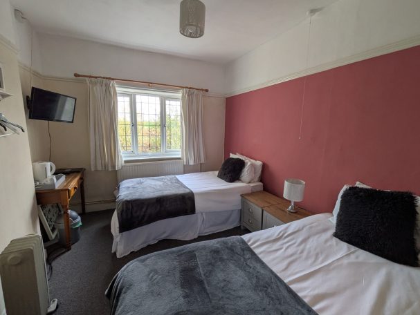 Large bedroom with two single beds, wall mounted TV and countryside view from window.
